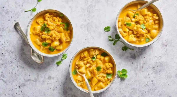 Trois bols de chou-fleur curry crémeux, garni de coriandre fraîche. Un plat réconfortant et savoureux.