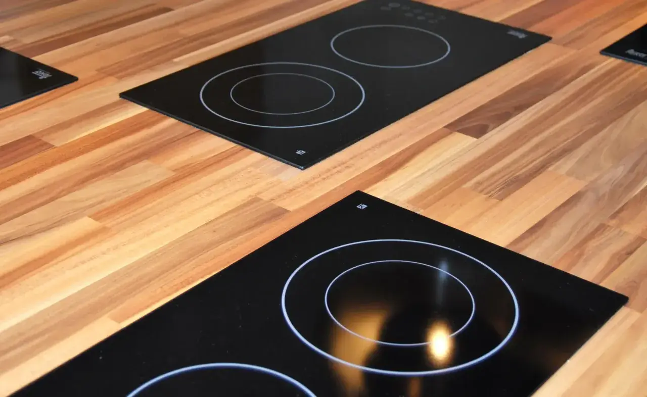 Plaques de cuisson modernes sur un plan de travail en bois. L'une est une plaque à induction ou vitrocéramique avec des cercles blancs.