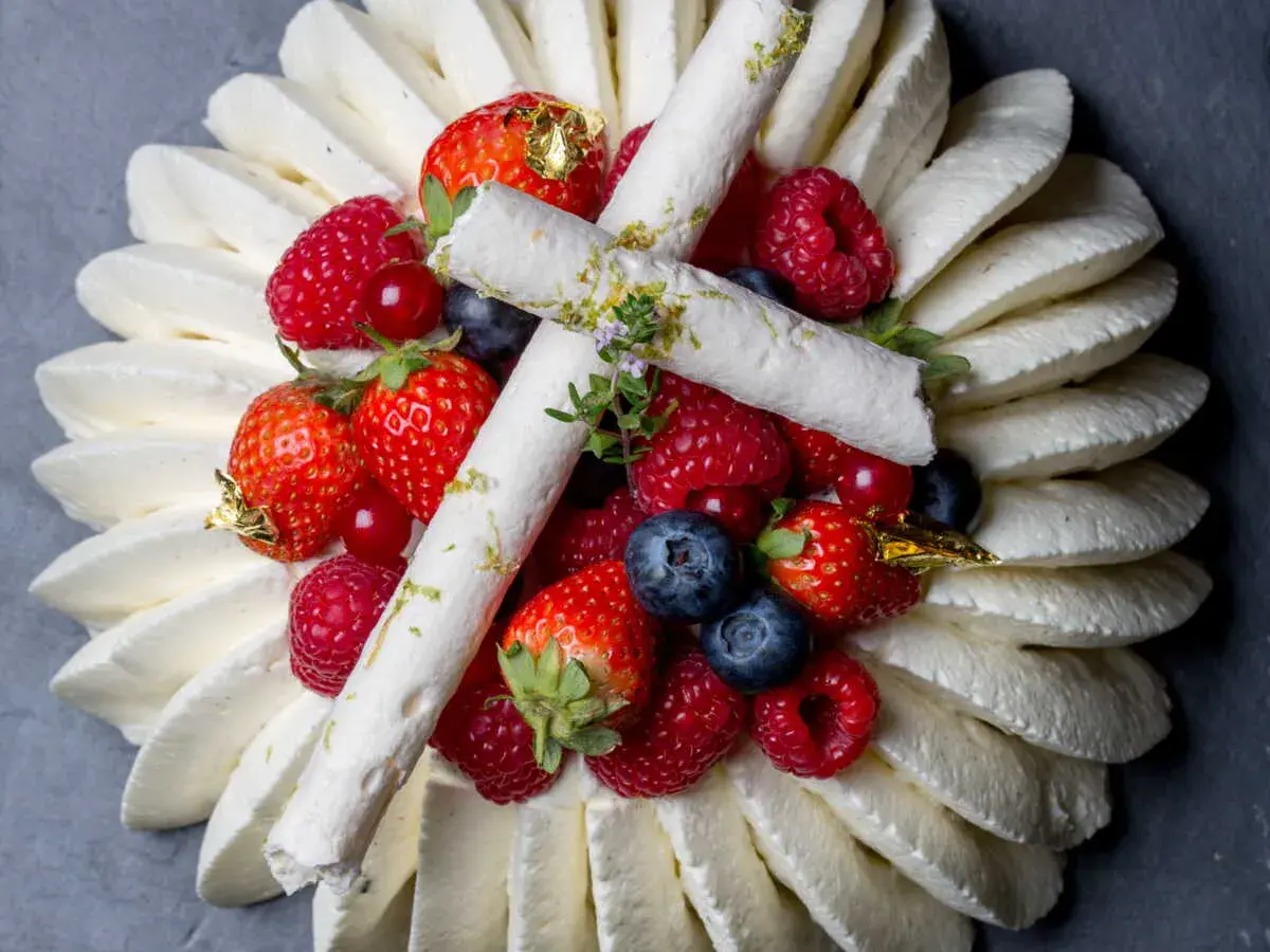 Pavlova aux fruits rouges, décorée de meringues fines et de feuilles d'or. Un délice visuel et gustatif.
