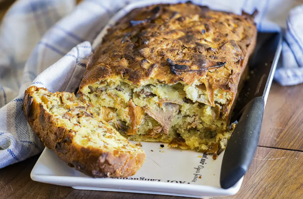 Un cake aux fanes de carottes, doré et moelleux, avec une tranche coupée, prêt à être dégusté.
