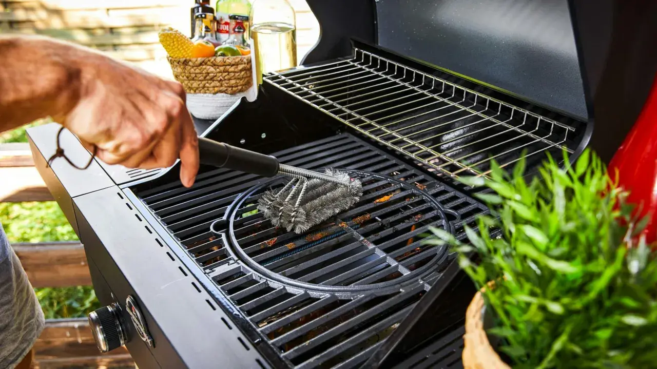 Main d'homme nettoyant une grille de barbecue avec une brosse métallique. Préparation pour la prochaine cuisson.
