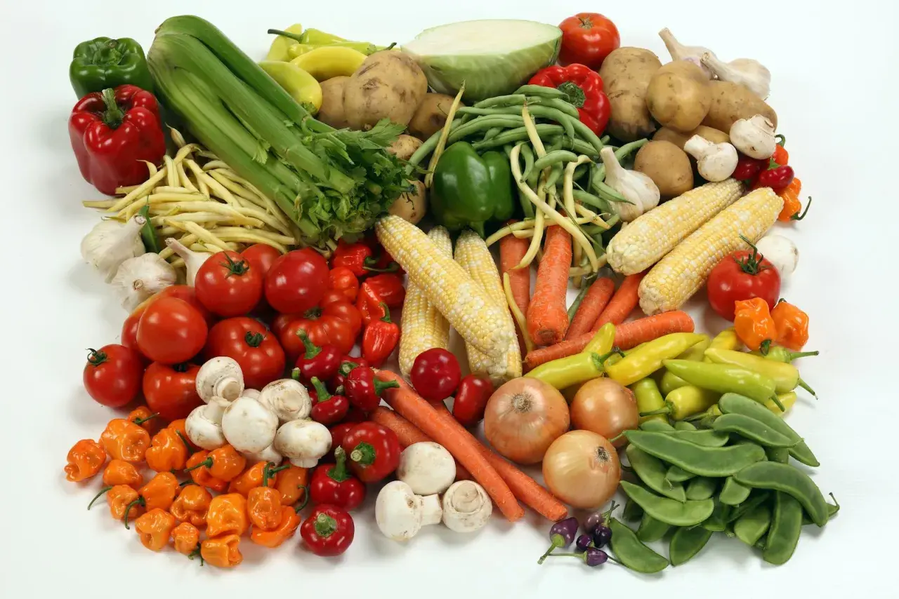 Un assortiment coloré de légumes frais : tomates, poivrons, carottes, maïs, oignons, champignons, ail, haricots verts et jaunes, et un chou. Un vrai festin de légume en b.
