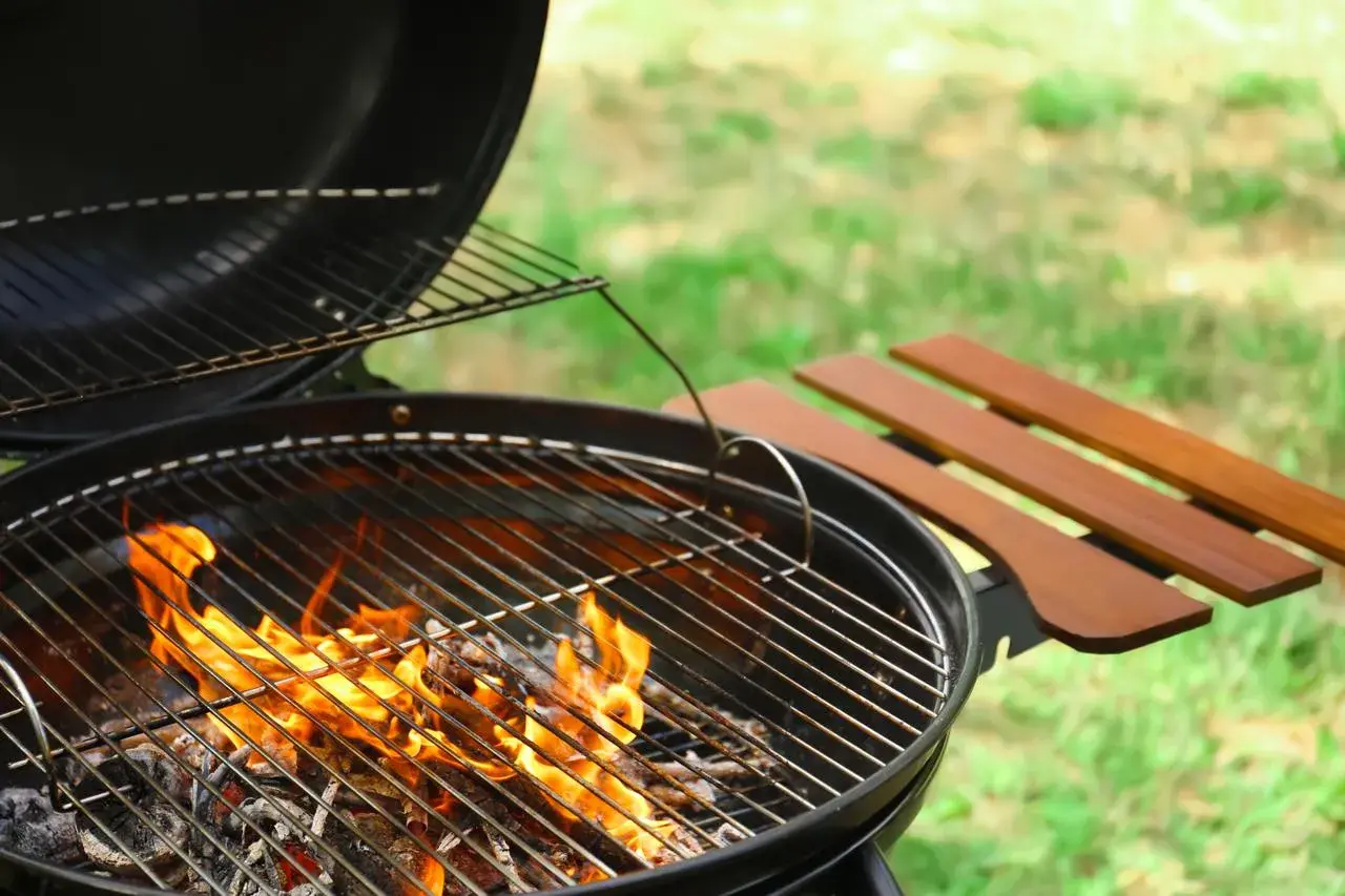 Le barbecue à charbon chauffe, les flammes dansent sur les braises. La température monte pour un repas d'été parfait.