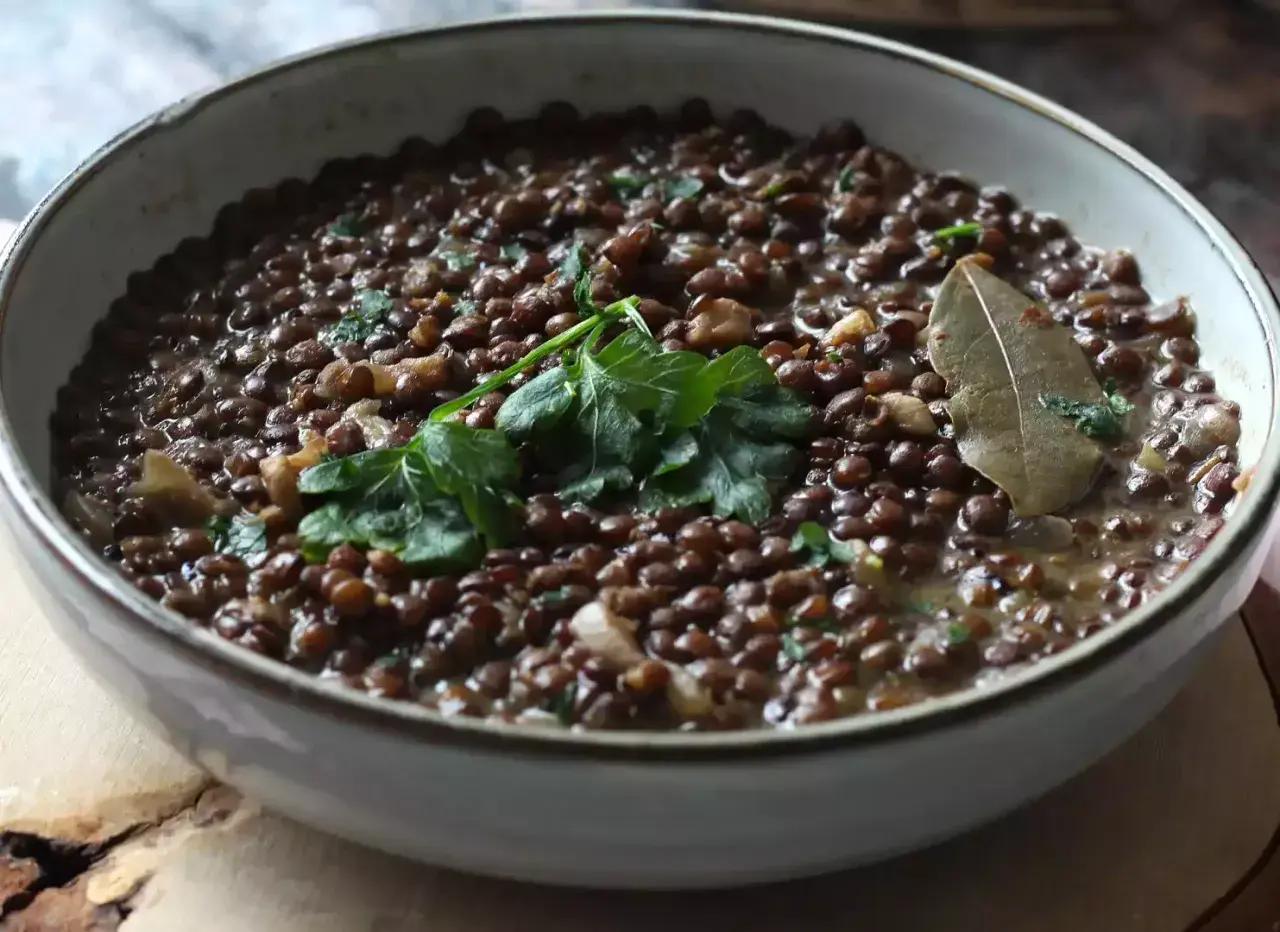 Un plat de lentilles vertes mijotées, garni de persil frais et d'une feuille de laurier. Parfait pour des recettes de lentilles vertes réconfortantes.
