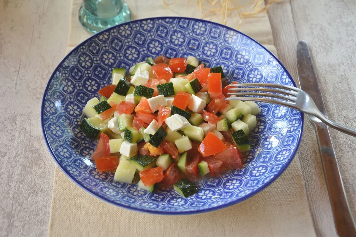 Salade de courgettes à la grecque, fraîche et colorée, avec des dés de tomates, courgettes et feta dans une assiette bleue.