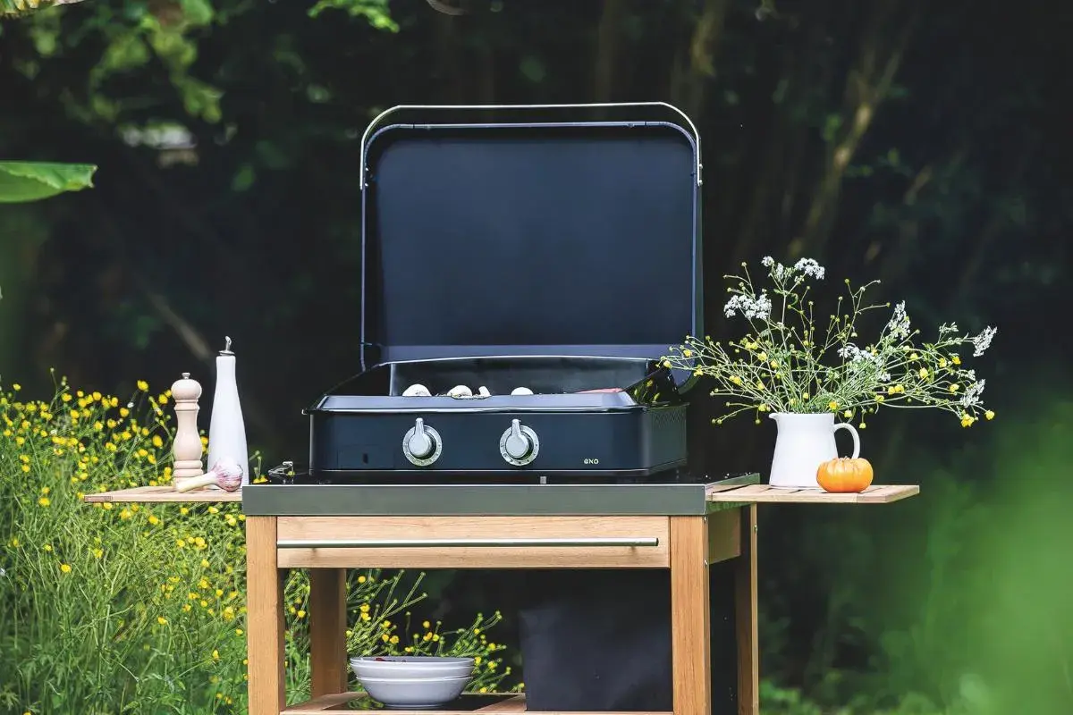 Plancha ou barbecue prêt pour un repas en plein air, avec des ingrédients sur le côté et un bouquet de fleurs sauvages.