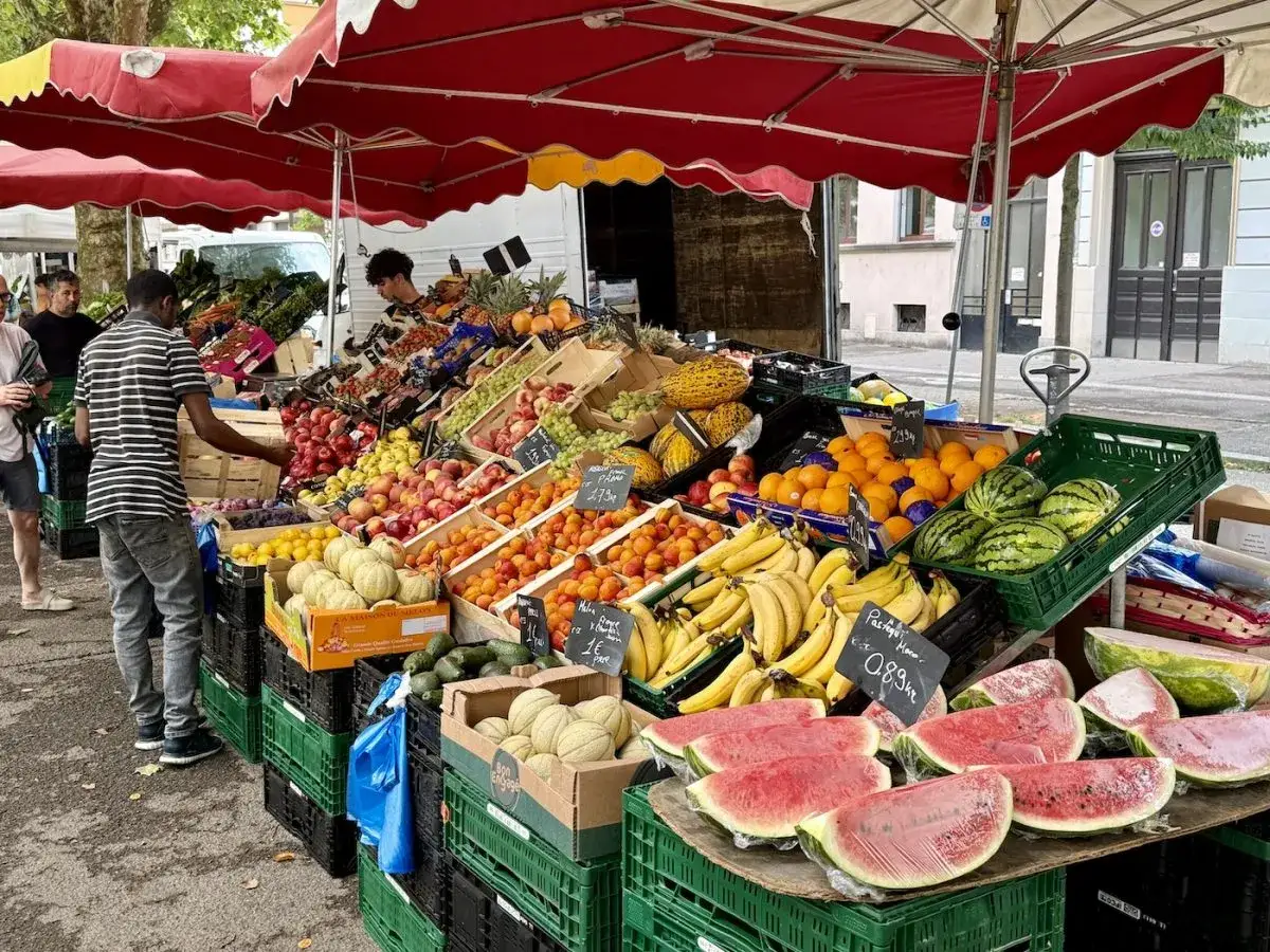 Un étal de marché débordant de fruits et légumes de saison : pastèques, bananes, pêches, abricots, melons, citrons et avocats.