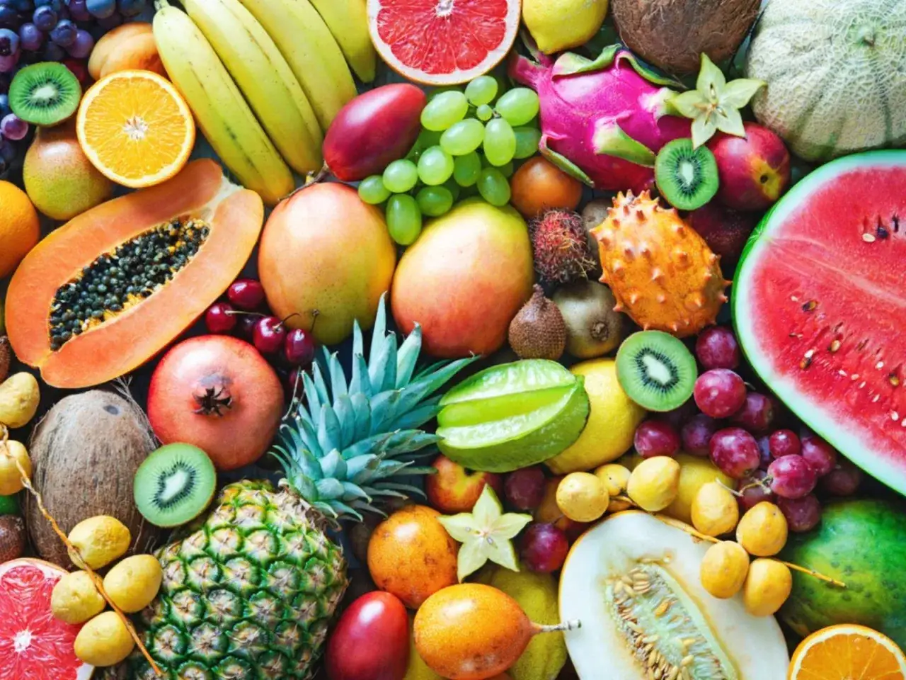 Un assortiment color&eacute; de fruits en vrac : past&egrave;que, ananas, papaye, mangues, raisins, kiwis, bananes, grenades, oranges, et plus encore.