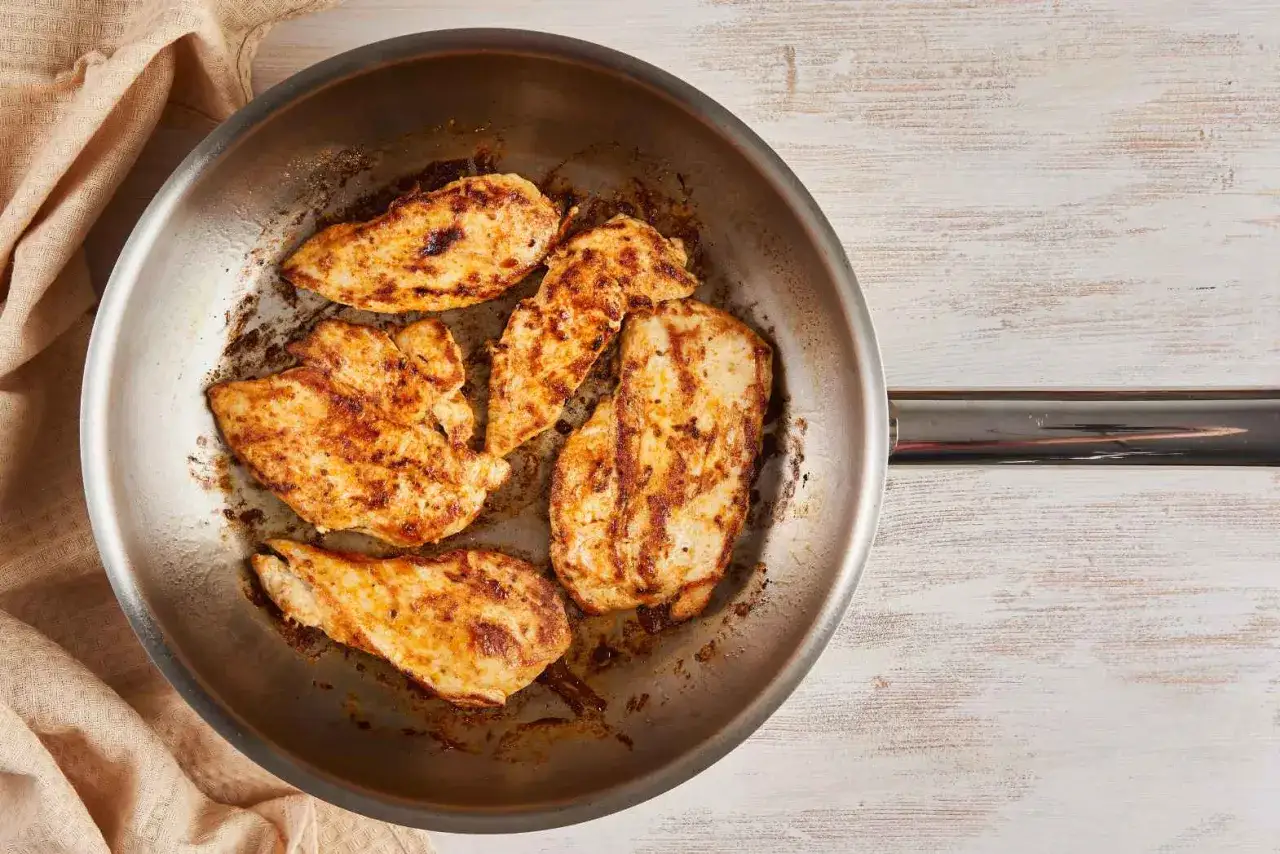 Poêle en acier inoxydable avec des morceaux de poulet grillés. Attention, la chaleur du poêle en acier inoxydable peut être un danger.