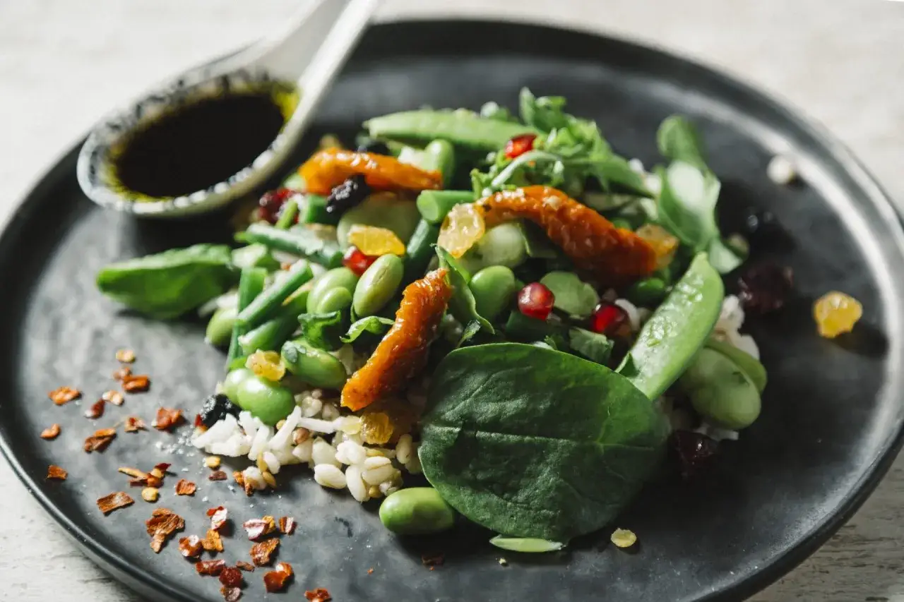 Une salade verte recette color&eacute;e avec des edamames, pois gourmands, tomates s&eacute;ch&eacute;es et grenade sur un lit de riz. Une cuill&egrave;re de sauce &agrave; c&ocirc;t&eacute;.