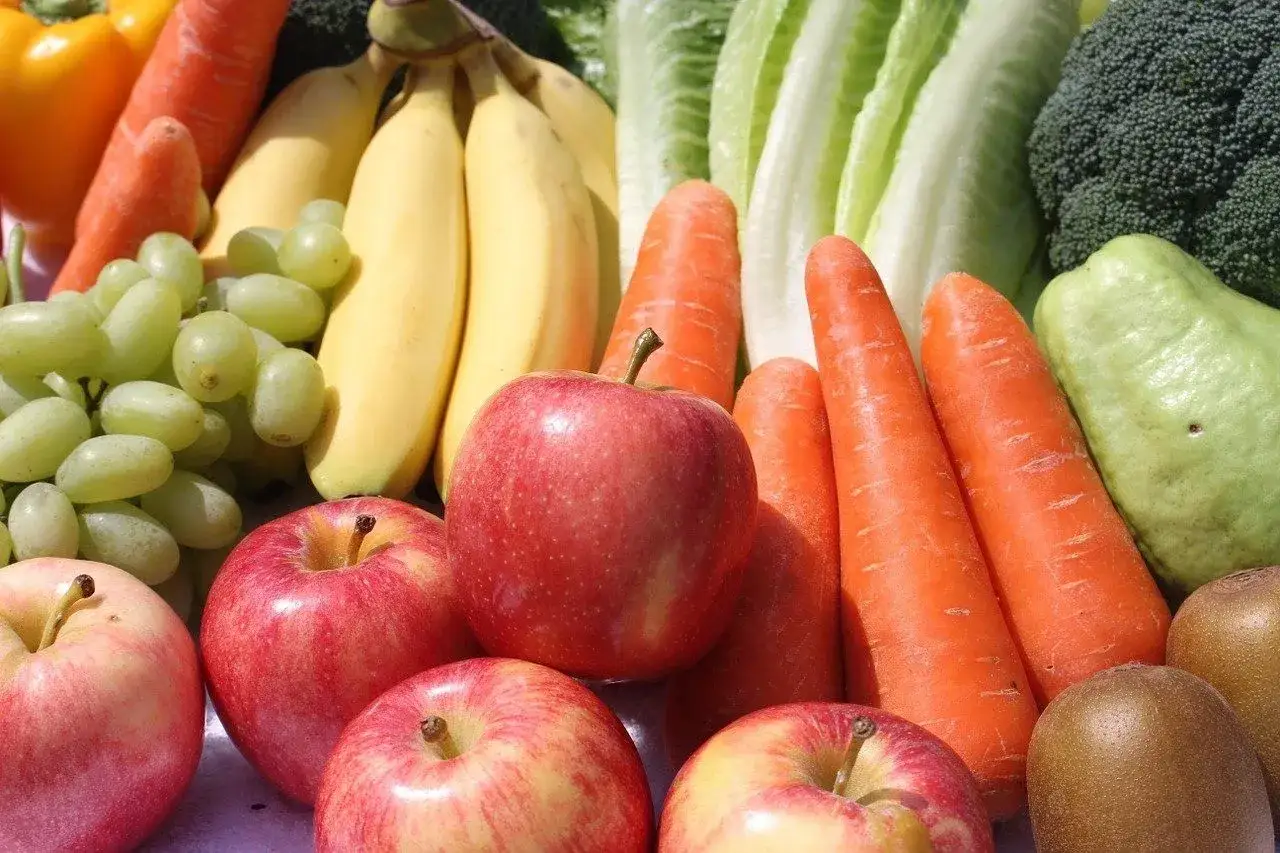 Un assortiment coloré de fruits et légumes en vrac : pommes rouges, bananes, raisins verts, carottes, brocolis, laitues et kiwis.