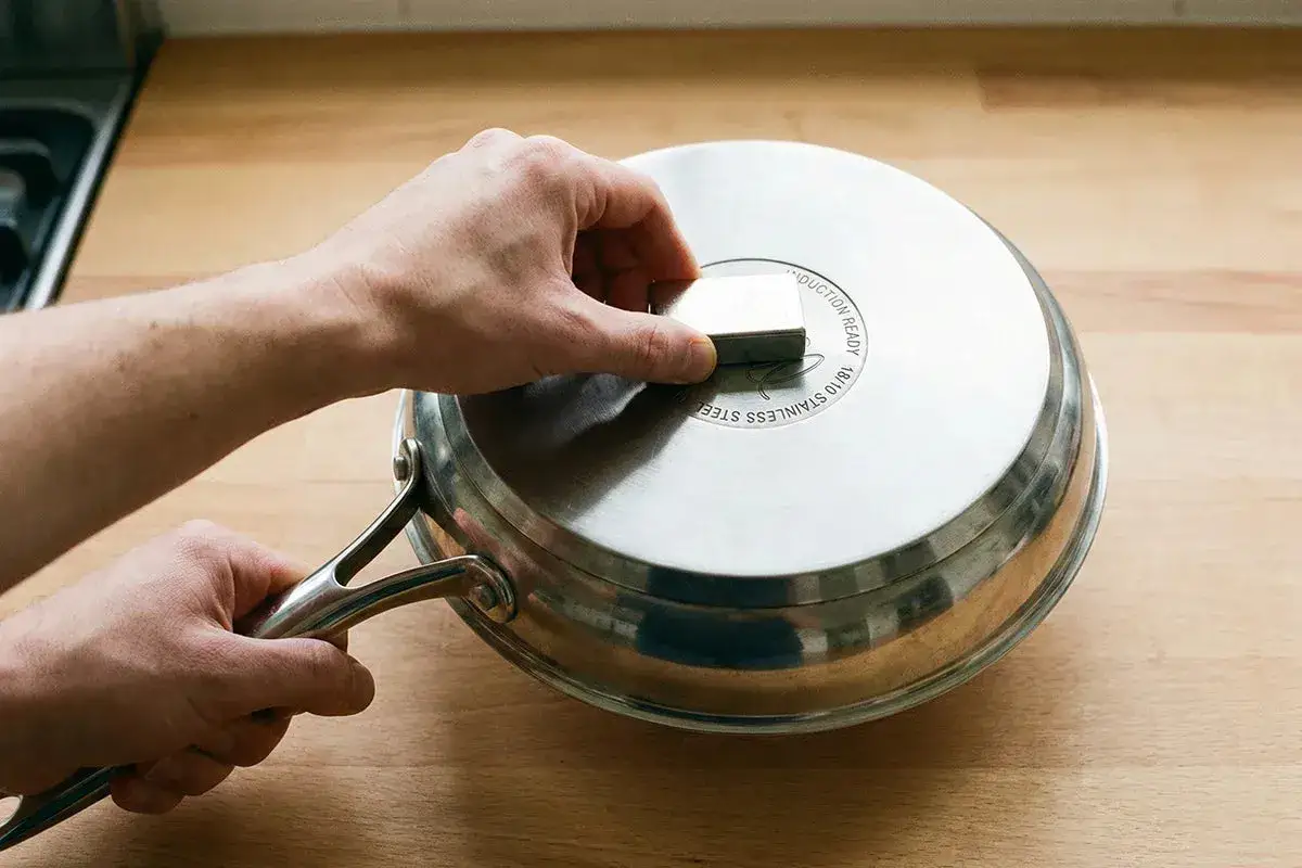 Une main teste avec un aimant si une casserole peut-on utiliser une casserole induction sur plaque électrique. Le fond indique 