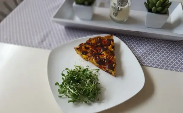Tranche de tarte aux poivrons colorée, servie avec une salade de pousses fraîches sur une assiette blanche.