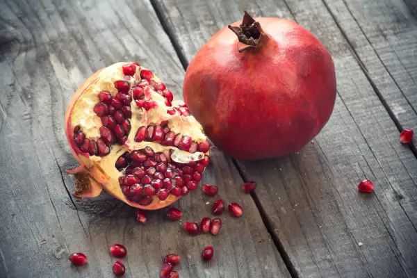 Une grenade entière et une ouverte, révélant ses arilles rouges éclatantes, sur un fond de bois vieilli. Un délice de la grenade fruit saison.