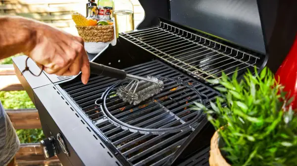 Main d'homme nettoyant une grille de barbecue avec une brosse métallique. Préparation pour la prochaine cuisson.