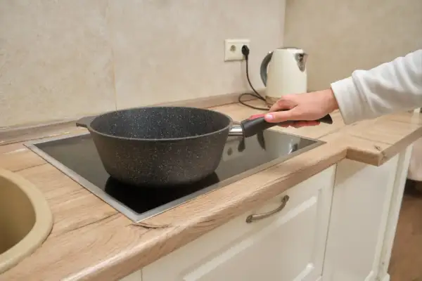 Une main tient une poêle sur une plaque de cuisson vitrocéramique, illustrant la différence entre plaque électrique et induction.