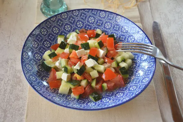 Salade de courgettes à la grecque, fraîche et colorée, avec des dés de tomates, courgettes et feta dans une assiette bleue.