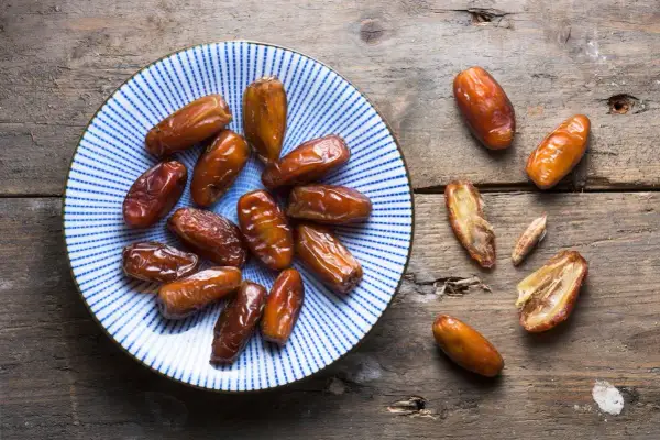 Assiette de dattes, un fruit en d. Ces fruits secs, brillants et caramélisés, sont disposés sur une assiette bleue et blanche et sur une table en bois rustique.
