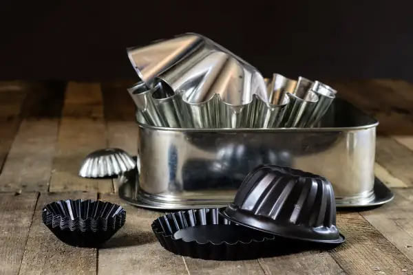 Un assortiment de moules à pâtisserie en acier, certains brillants, d'autres noirs. Attention, le moule en acier peut être dangereux si mal utilisé.
