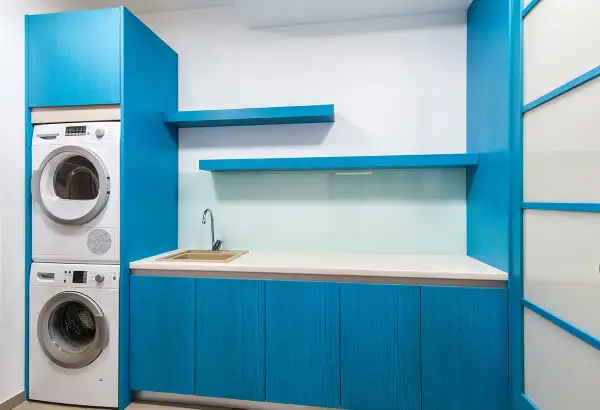 Espace buanderie moderne avec lave-linge et sèche-linge superposés, évier et placards bleus.