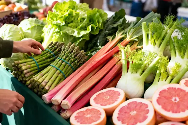 Un étal de marché débordant de fruits et légumes de saison : asperges, rhubarbe, fenouils, laitues et pamplemousses coupés.
