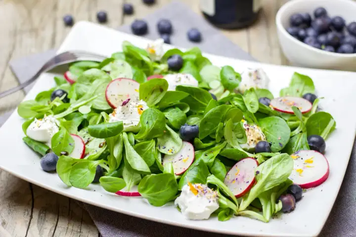 Salade verte fraîche avec radis, myrtilles et fromage frais. Une idée de quoi mettre dans une salade verte pour un repas léger et coloré.
